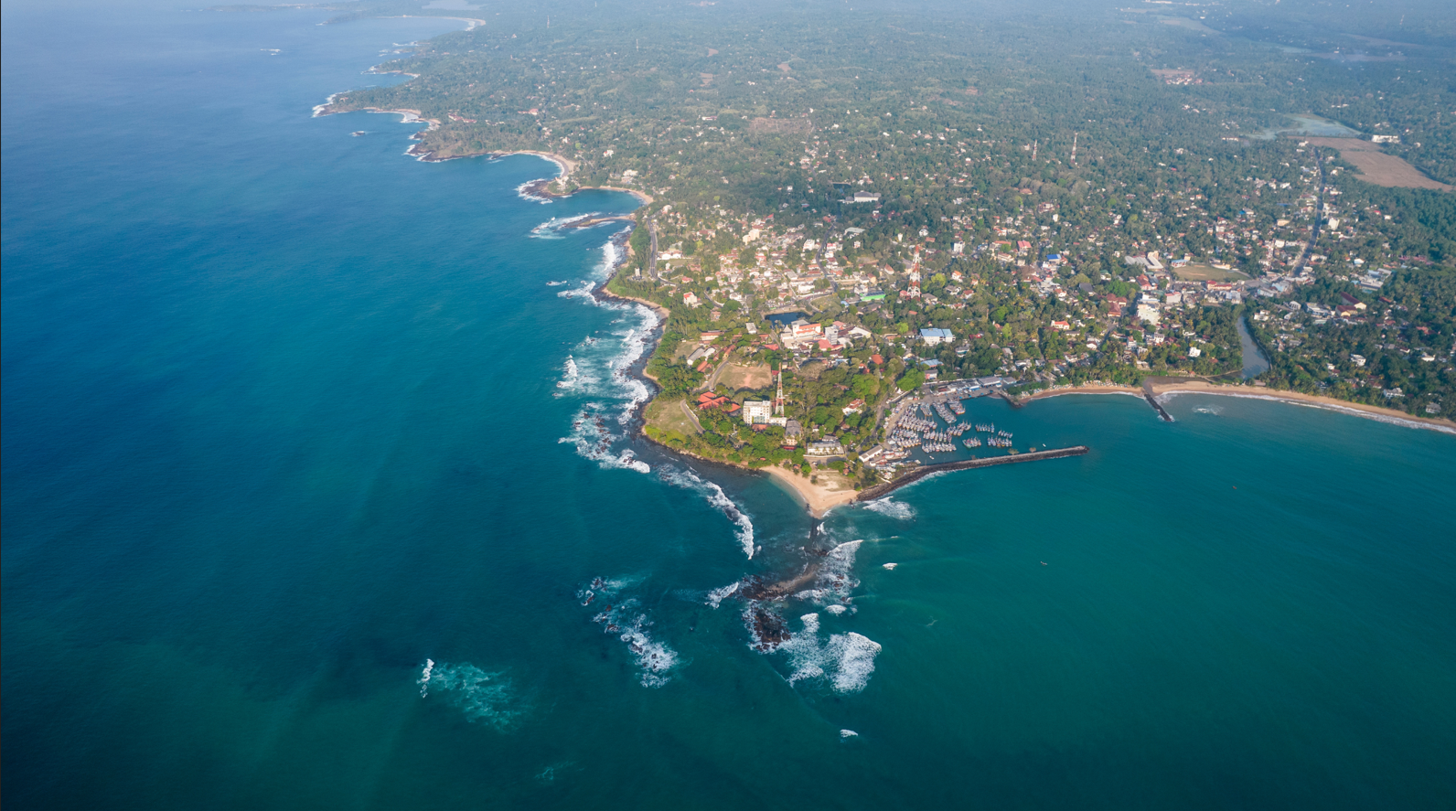 Aeriall photograph of a coastal peninsula with urban development , winding roads, green spaces and deep blue waters