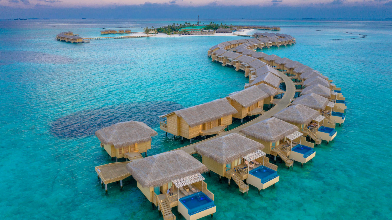 Aerial view of Maldives overwater villas with turquoise water and sunset sky